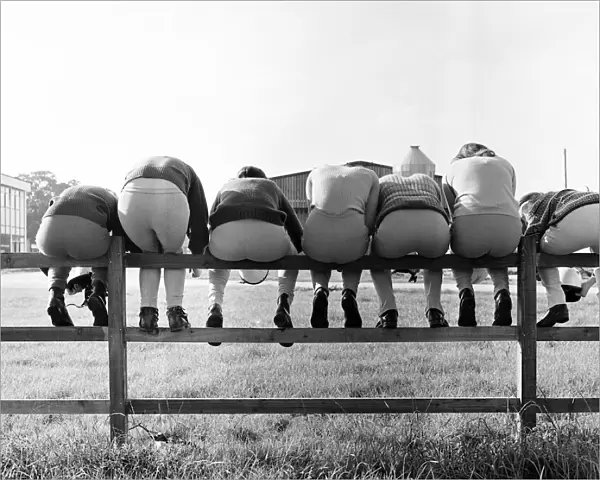 Seven young apprentice female jockeys sitting on a wooden fence during their training at