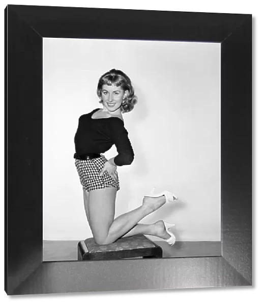 A model wearing a jumper and shorts, posing on a stool. 1954