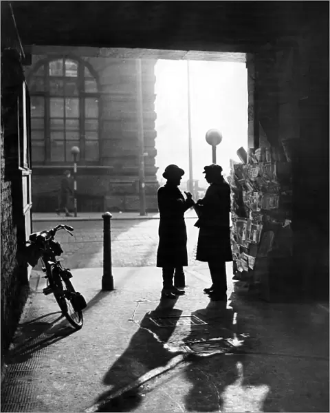 A man talking to a newspaper seller under the covered entrance to Leather Lane