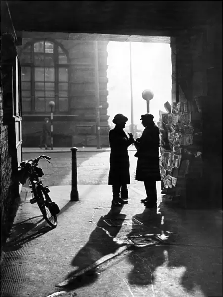 A man talking to a newspaper seller under the covered entrance to Leather Lane