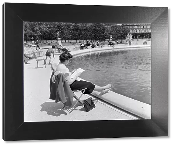 France Paris - A lady sits resting her feet beside a pond in a park reading a letter