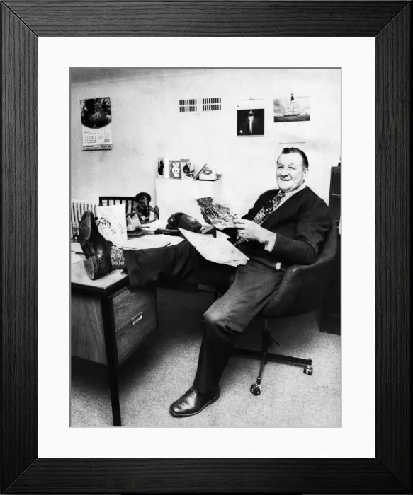 Framed Print : Liverpool manager Bob Paisley looking relaxed with his leg on the desk as he reads Framed Print : Liverpool manager Bob Paisley looking relaxed with his leg on the desk as he reads