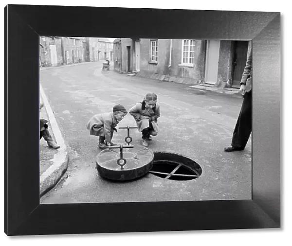 Children looking down a drain hole in the road in Thornbury, South Gloucestershire