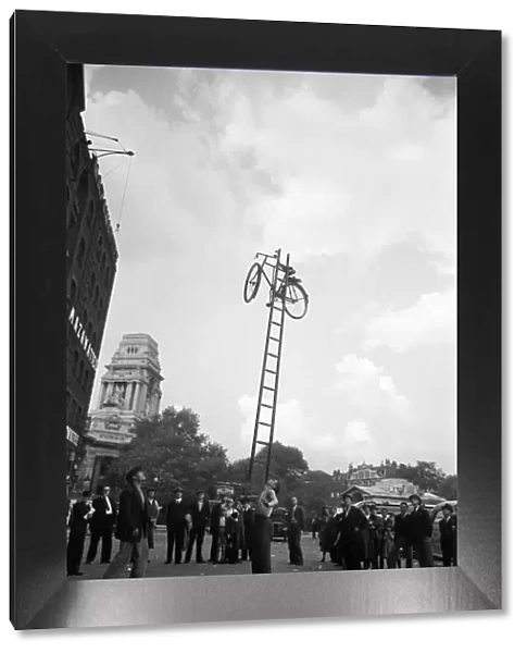 A street entertainer at Tower Hill, London balancing a bicycle on a ladder using his chin