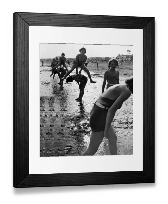 Framed Print : Women and children playing leap frog on the beach. Eastney