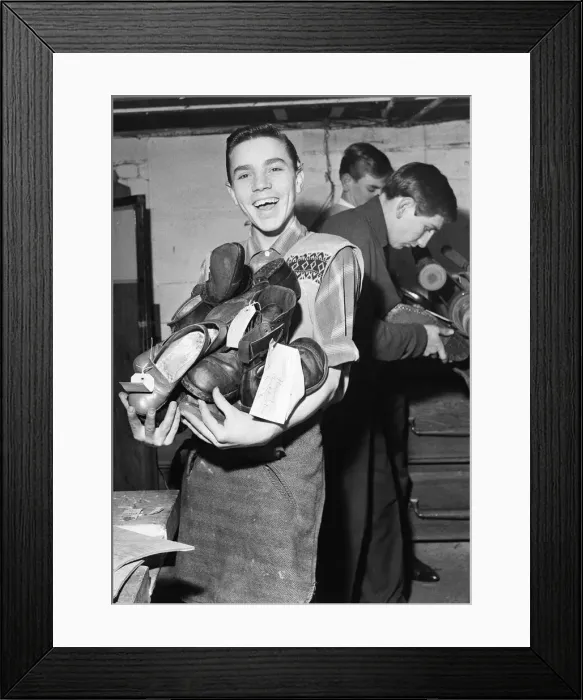 Framed Print : A boy carries a bundle of shoes. He is at work