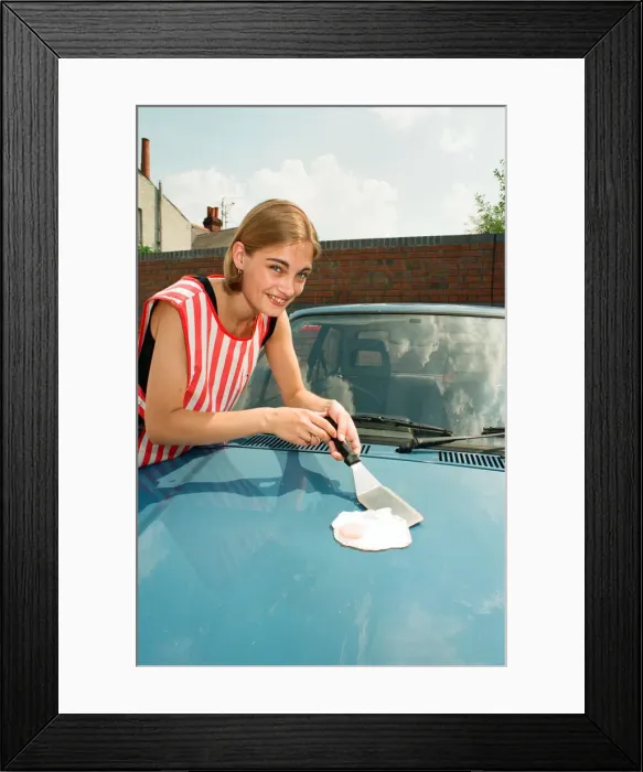 Framed Print : A girl frying an egg on a car bonnet during the 1995 heatwave. 1st August 1995