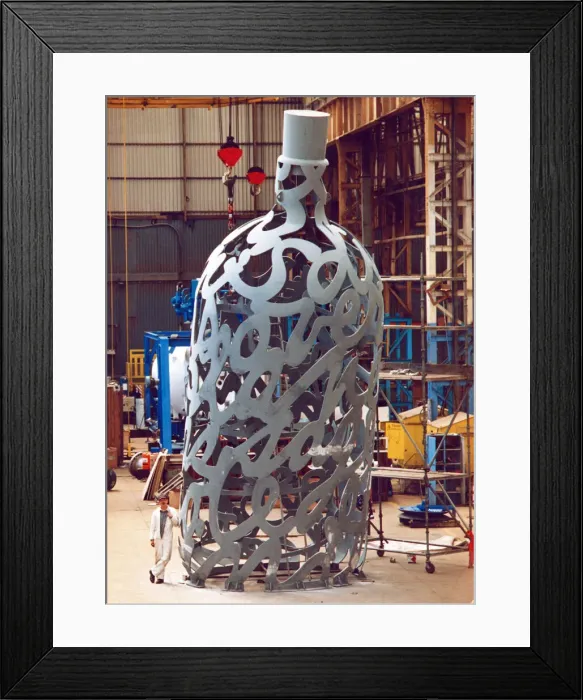 Framed Print : Yard electrician Peter Gilpin is dwarfed by the huge 35 foot metal bottle ordered by Framed Print : Yard electrician Peter Gilpin is dwarfed by the huge 35 foot metal bottle ordered by