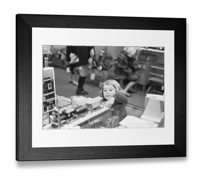 Framed Print : Small girl looks on longingly at the latest Lego set in the toy department of Heelas