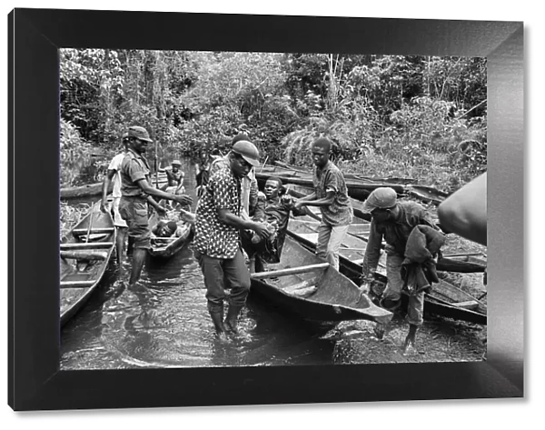 Biafran soldiers and helpers seen here carrying an injured comrade onto a canoe to cross