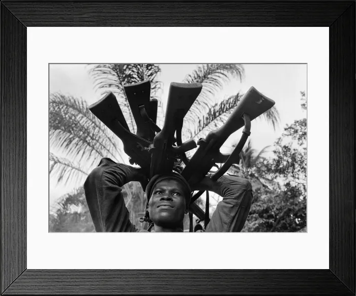 Framed Print : A Biafran soldier seen here holding a selection of guns during the Biafran conflict Framed Print : A Biafran soldier seen here holding a selection of guns during the Biafran conflict