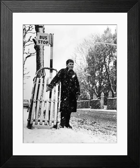 Framed Print : Young Andrew Burley stands in the queue for the bus with his sledge during heavy snowfall Framed Print : Young Andrew Burley stands in the queue for the bus with his sledge during heavy snowfall