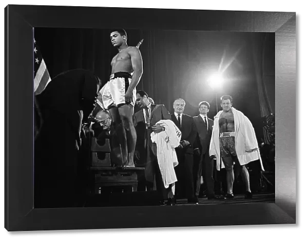 Muhammad Ali stands on the scales as Brian London looks on at the weigh-in ahead of their