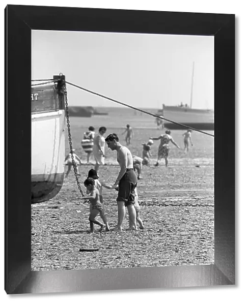 A father with his young family seen here exploring the mud flats at Southend, Essex