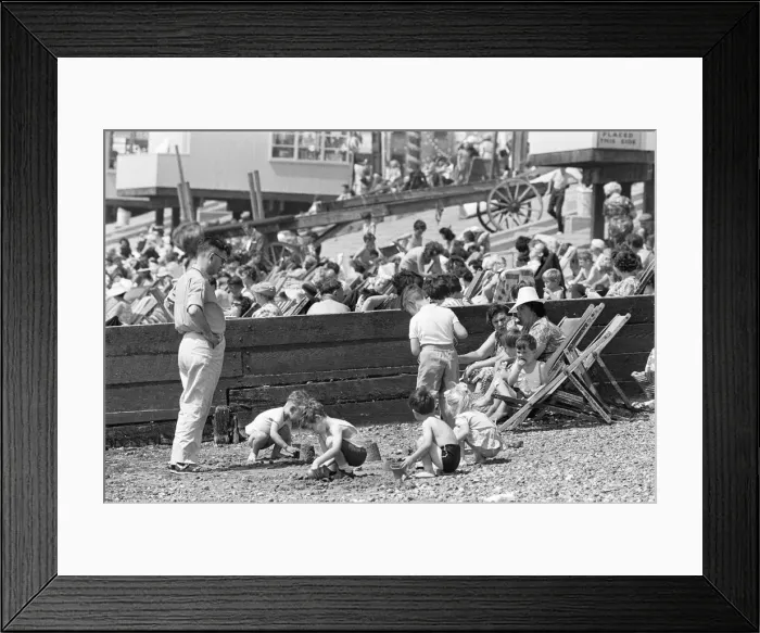 Framed Print : Mum enjoys a sandwich and dad looks on as children build sand castles on the beach