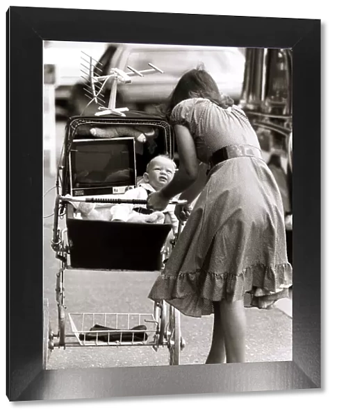 Unusual - Mother pushing a pram with her baby and a portable television set placed next