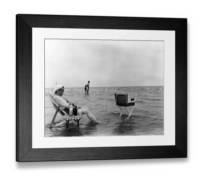 Framed Print : A seaside scene of a man watching television on the beach. Littlehampton, West Sussex
