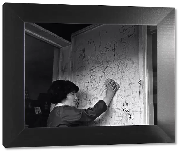A shop assistant removes the scribbling on the wall outside her shop in Kirkby, Liverpool