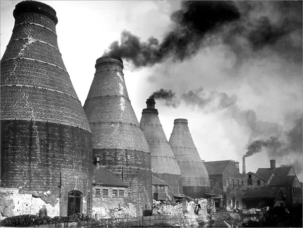 A smokey view with the typical scene of bottle ovens and kilns during the industrial