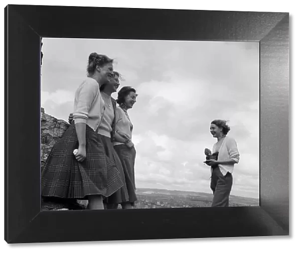 A woman taking a photograph of three women, in a coastal area, North Yorkshire