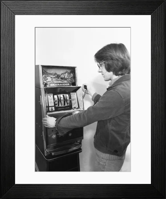 Framed Print : Man playing a one arm bandit slot machine in a London amusement arcade. 8th January 1975 Framed Print : Man playing a one arm bandit slot machine in a London amusement arcade. 8th January 1975