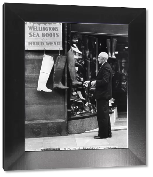 May 1950. Alderman TR Broadbent looking at a shop display of boots outside a shop by