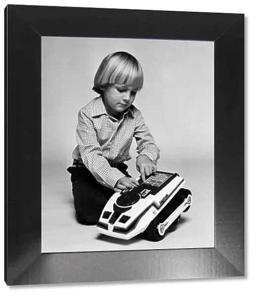 A young boy playing with a Big Trak toy, a programmable electric vehicle created by