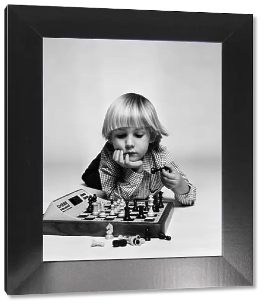 A young boy playing with 'Chess Challenger', an electronic chess game