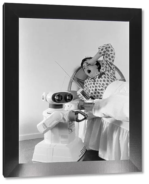 A young boy in bed being woken by an Omnibot 2000 toy robot. 21st October 1986