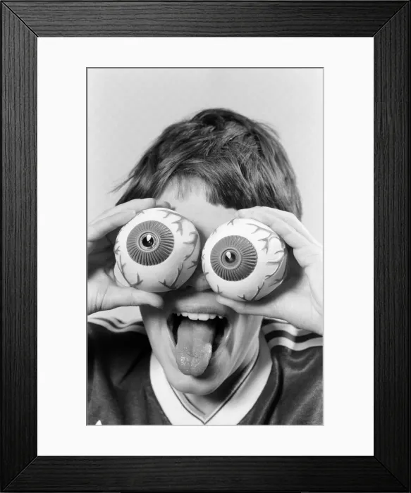 Framed Print : A young boy holding fake eye ball toys up to his eyes. 21st October 1986