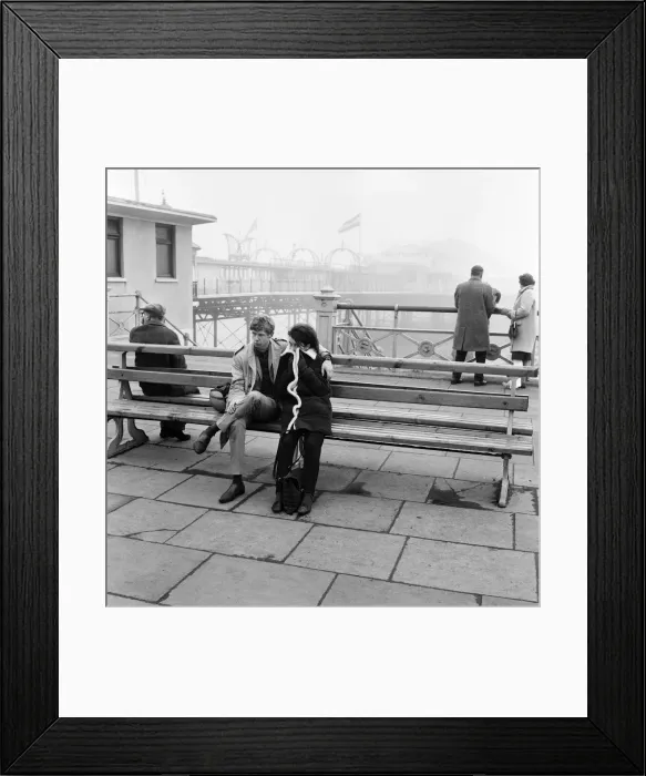 Framed Print : A couple dressed up and cuddled up to resist the cold on the Brighton front by the pier Framed Print : A couple dressed up and cuddled up to resist the cold on the Brighton front by the pier