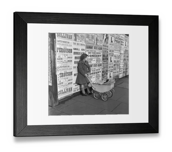 Framed Print : Little girl with toy pram stands waiting for her mother against a background of adverts Framed Print : Little girl with toy pram stands waiting for her mother against a background of adverts