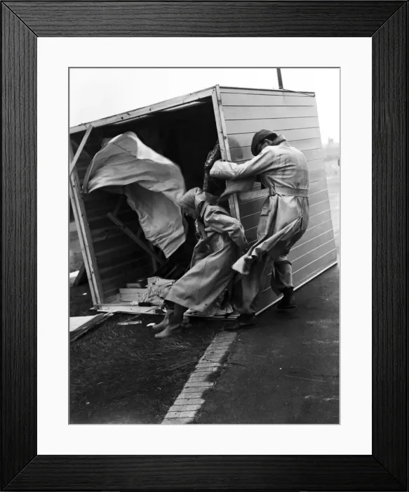 Framed Print : Gale damage. A couple cling desperately to their overturned beach hut at Littlehampton to
