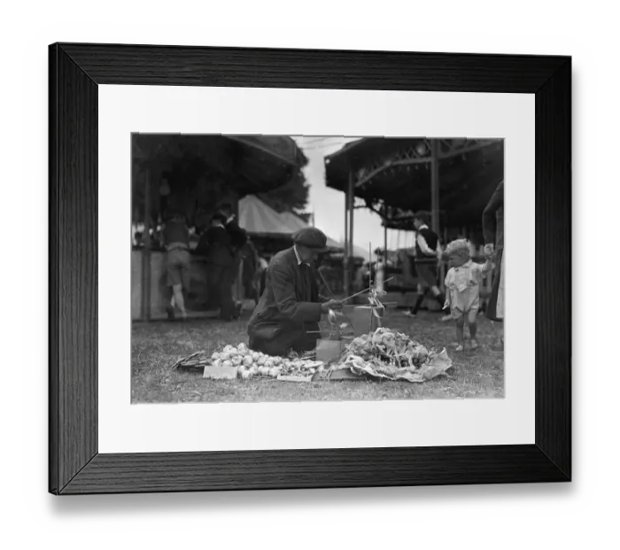 Framed Print : A toddler looks on in curiosity as a fancy goods vendor prepares his goods for sale