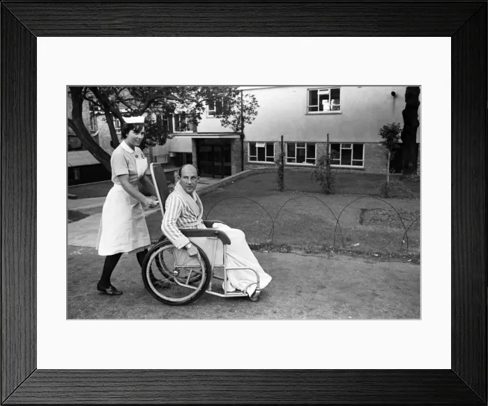 Framed Print : Stirling Moss, pictured in a wheelchair being pushed by a nurse Framed Print : Stirling Moss, pictured in a wheelchair being pushed by a nurse