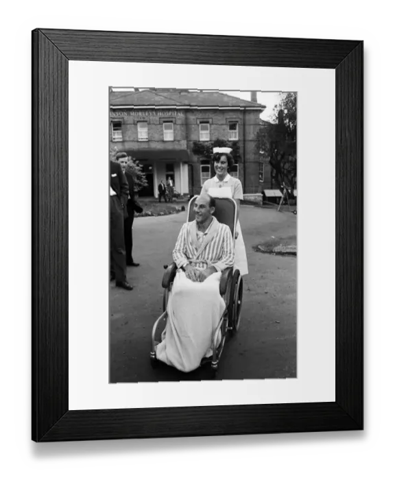Framed Print : Stirling Moss, pictured in a wheelchair being pushed by a nurse