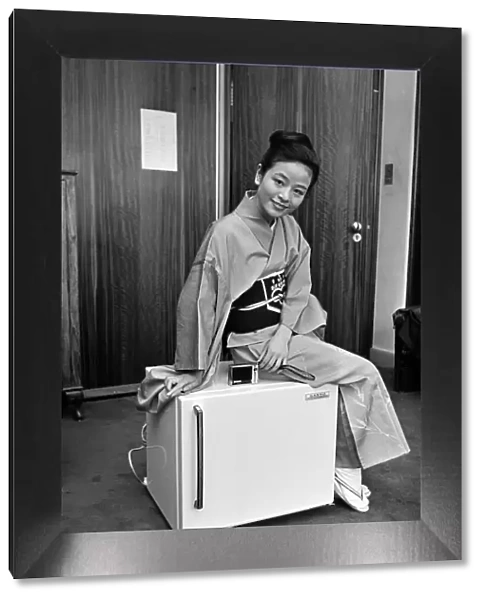 A woman wearing a Kimono sitting on a Japanese food freezer. 26th July 1965