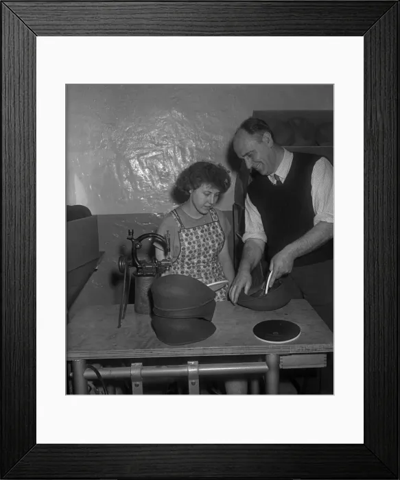 Framed Print : A new employee being shown how to insert a inner liner into a flat cap at the Denham Framed Print : A new employee being shown how to insert a inner liner into a flat cap at the Denham