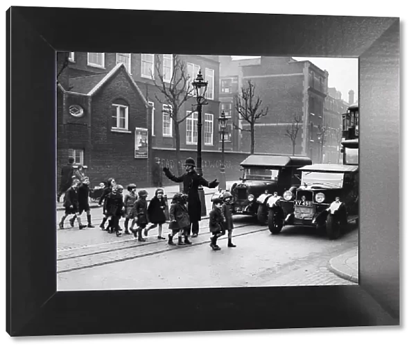 A policeman helping children to cross the road. London, February 1934