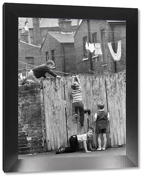 Children playing in the streets, climbing a fence. June 1964