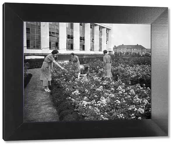 Female Hoover factory workers in a flower garden outside the factory building