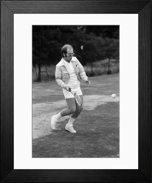 Framed Print : Elton John playing tennis on an outer court at Wimbledon. 25th June 1974