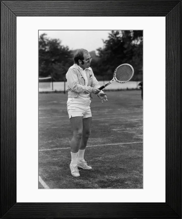 Framed Print : Elton John playing tennis on an outer court at Wimbledon. 25th June 1974