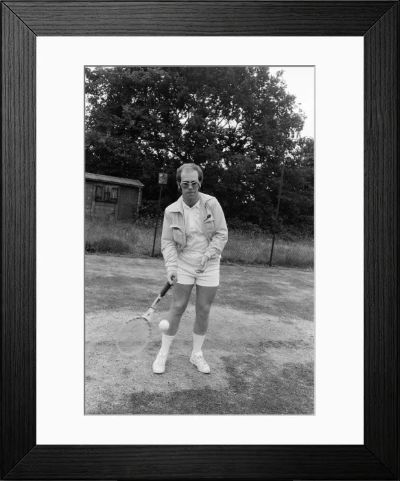 Framed Print : Elton John playing tennis on an outer court at Wimbledon. 25th June 1974