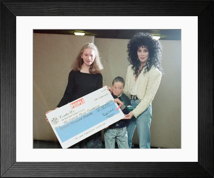 Framed Print : Cher, American singer, presents cheque for 15, 000 pounds to representatives of