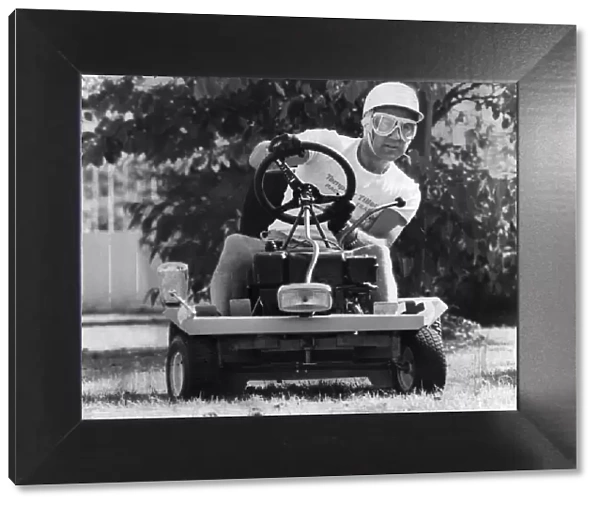 Stirling Moss sitting on lawn mower wearing crash helmet