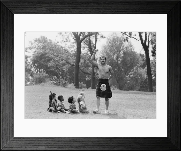 Framed Print : John Conteh gets the Scottish flavour on Parliament Hill Fields today watched by curious