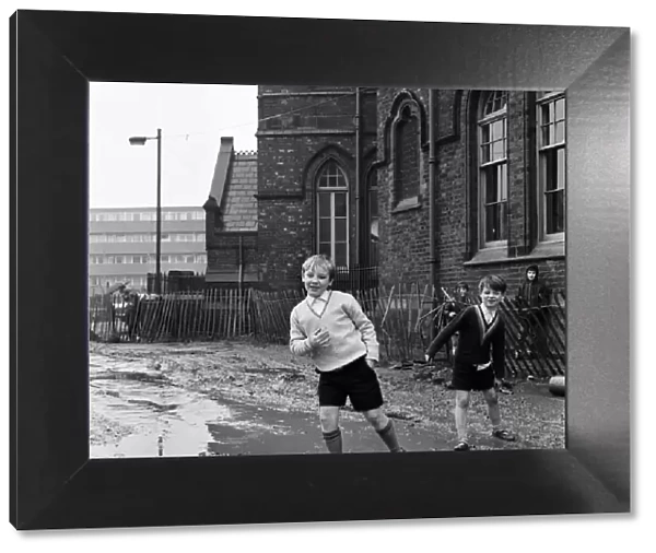 Two pupils of Ross Place School, Ardwick, Manchester, jump across a sea of mud to enter