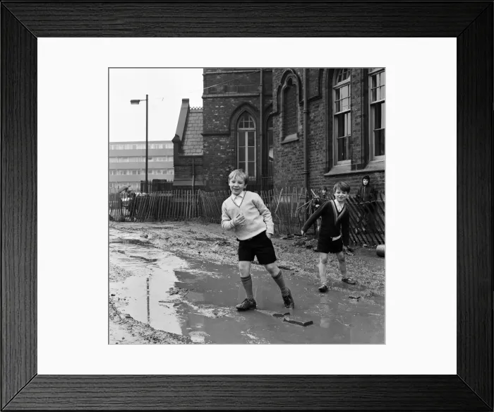 Framed Print : Two pupils of Ross Place School, Ardwick, Manchester, jump across a sea of mud to enter Framed Print : Two pupils of Ross Place School, Ardwick, Manchester, jump across a sea of mud to enter