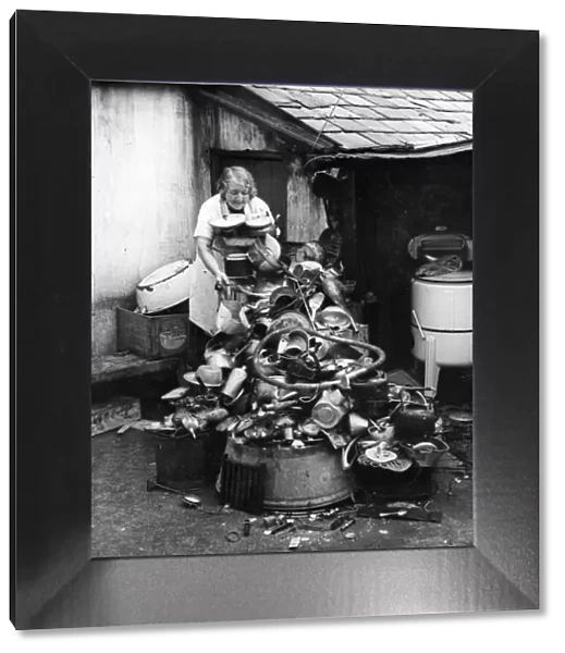 Picture shows a lady salvaging a variety of goods, such as pots and pans, plates, china